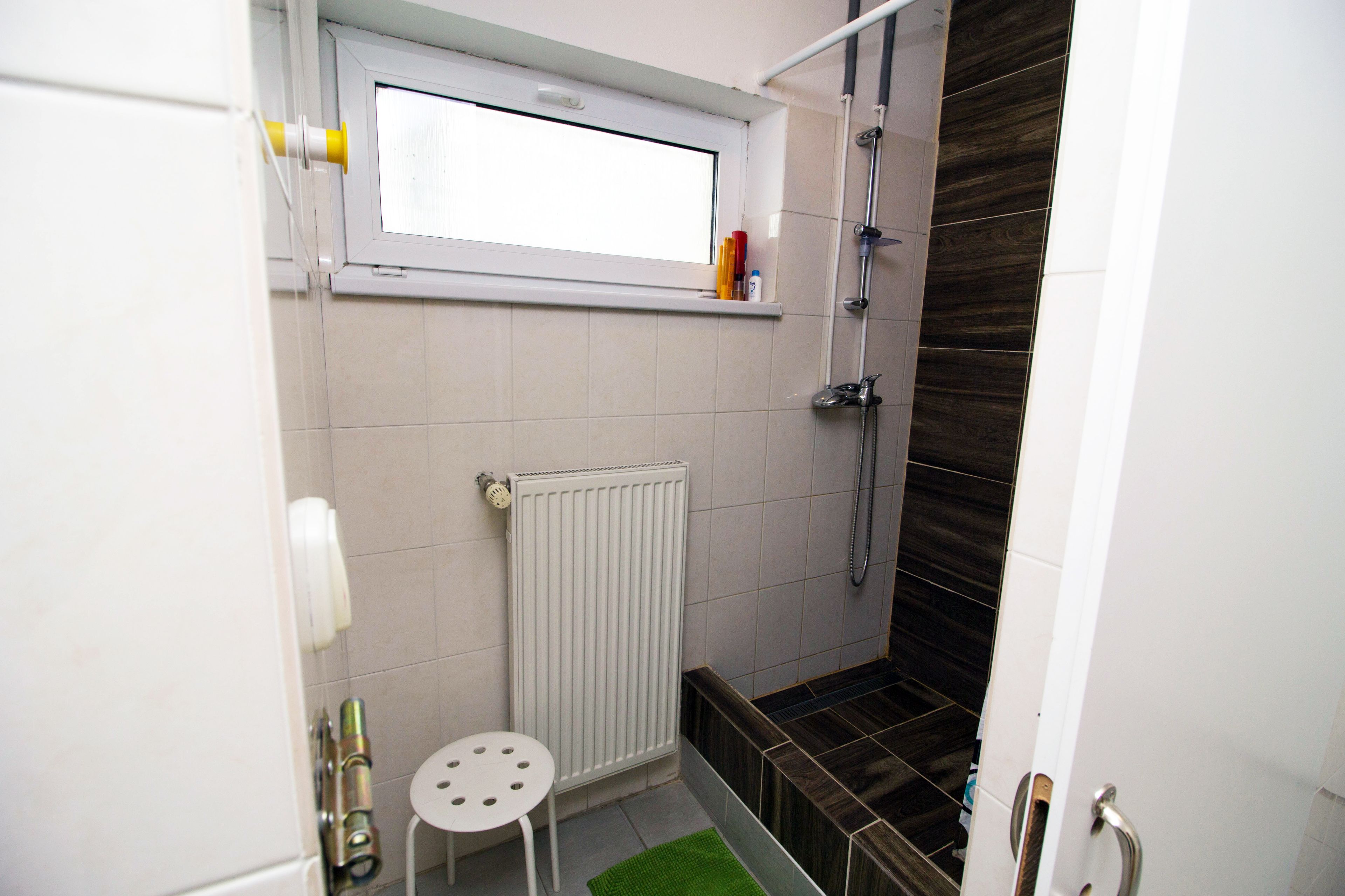 Un baño pequeño con ventana, radiador, ducha y retrete.