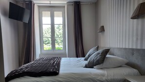 Ein Schlafzimmer mit einem Bett, einem Nachttisch, einem an der Wand befestigten Fernseher und einem Fenster mit Vorhängen.