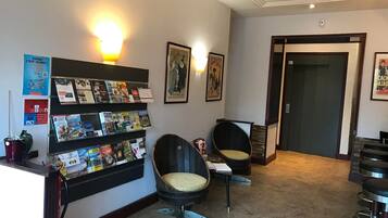 A reception area with a wall-mounted information board, two cushioned chairs, a bar area, and a door.