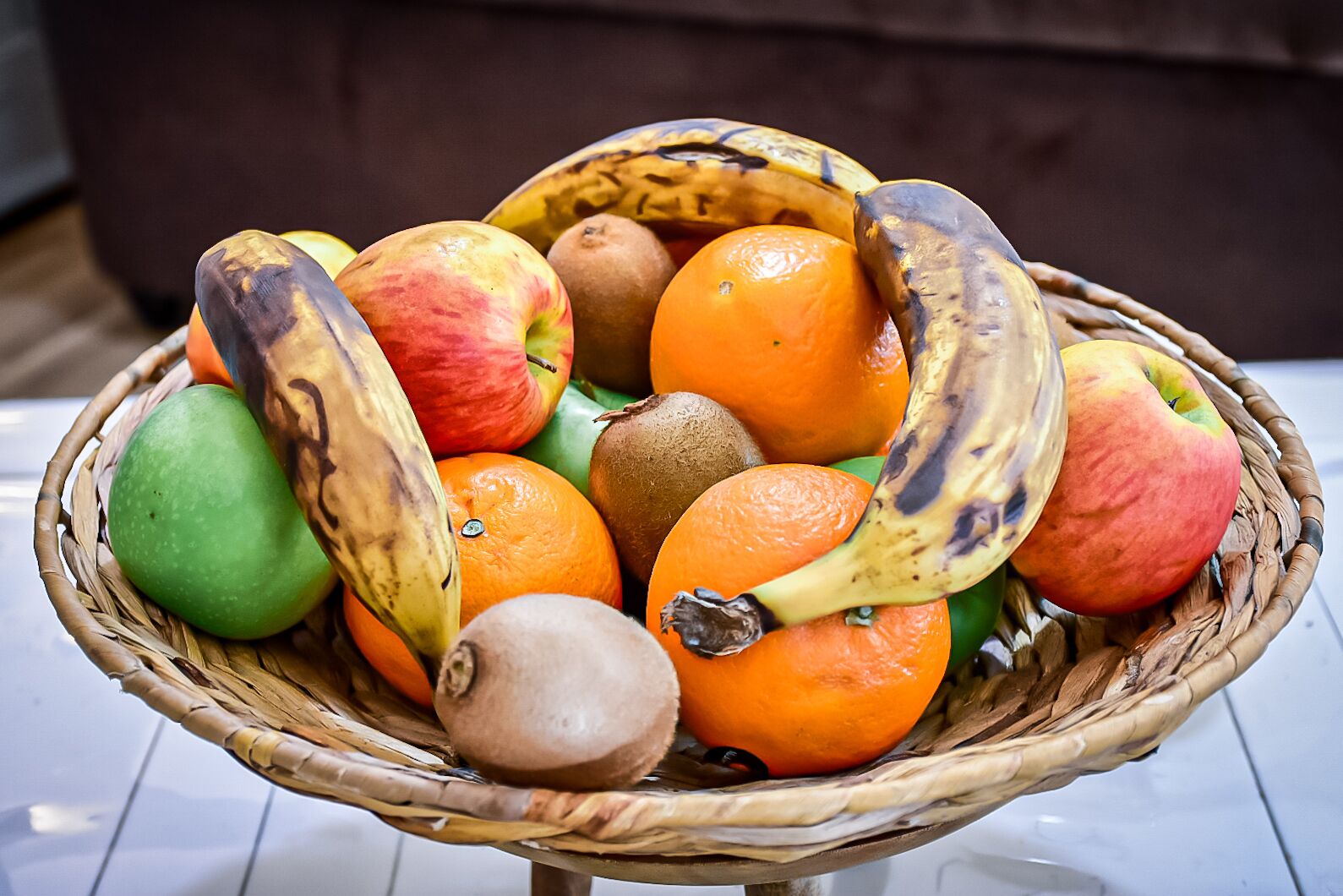Una cesta de mimbre llena de frutas variadas como manzanas, naranjas, plátanos y un kiwi.