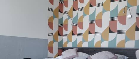 Camera da letto moderna con un letto, testiera imbottita grigia e parete decorata.