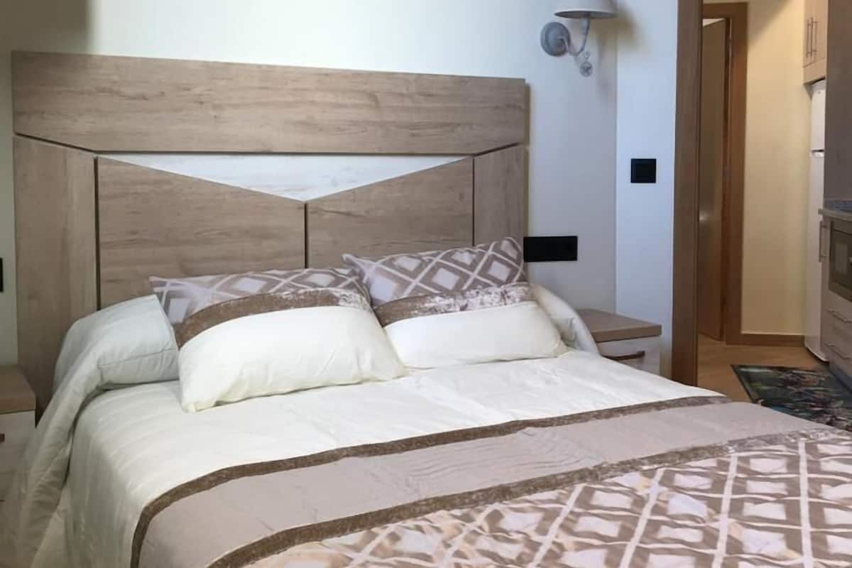 Cama bem arrumada com cabeceira de madeira, abajur e colcha estampada.