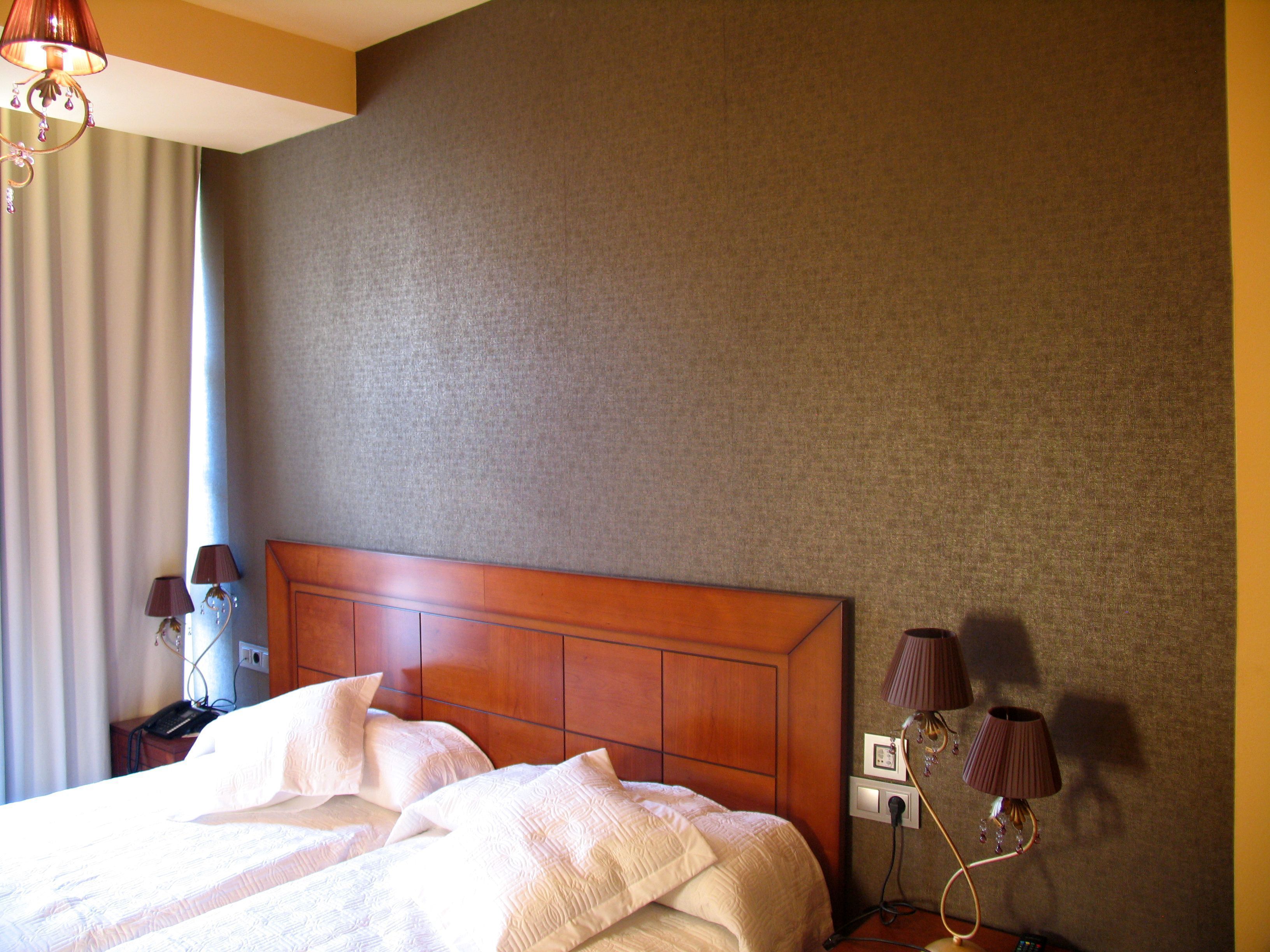 Una habitación de hotel con una cama grande, cabecera de madera, dos lámparas de noche y un teléfono instalado en la pared.