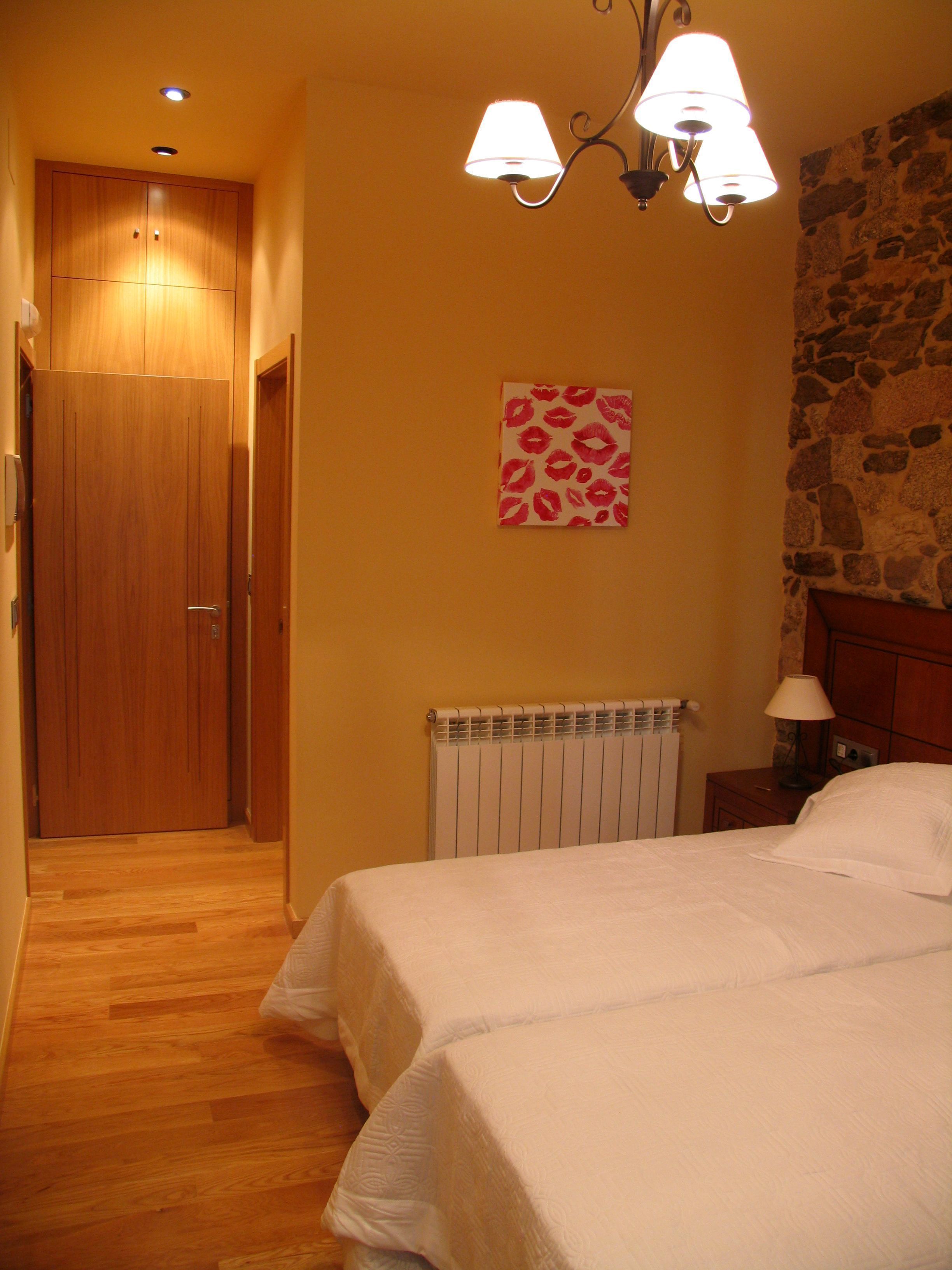 A bedroom with a wooden door, a radiator, a stone wall, and a bed with a white bedspread.