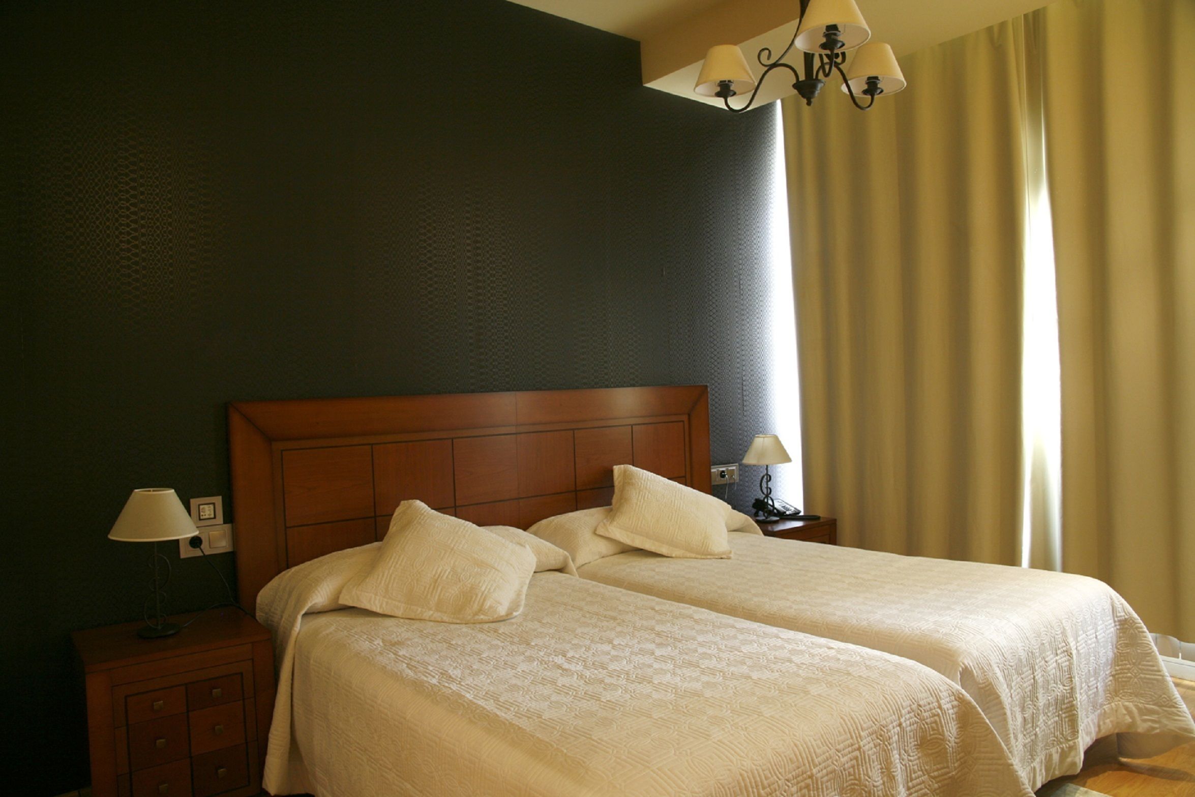 Una cama doble con cabecera de madera, dos mesitas de noche con lámparas y una ventana con cortinas.
