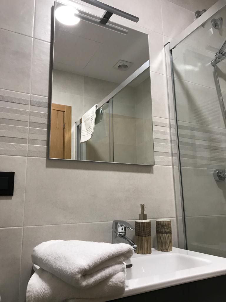 Un baño con espejo, lavamanos, toalla y cabina de ducha.