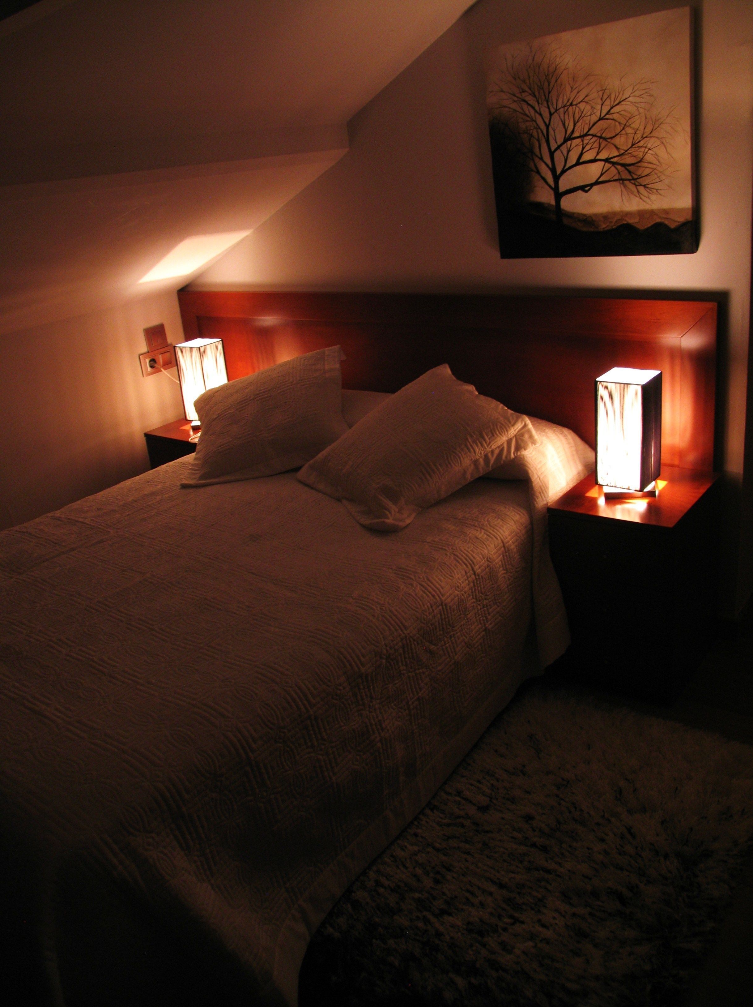 A dimly lit hotel room with a large bed, two bedside lamps, and a painting on the wall.