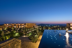 Un resort con una amplia piscina infinita, senderos bien iluminados y vistas a montañas distantes.