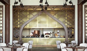 A restaurant with a central kitchen, wooden lattice partition, and white chairs. - Anantara Al Jabal Al Akhdar Resort (Nizwa)
