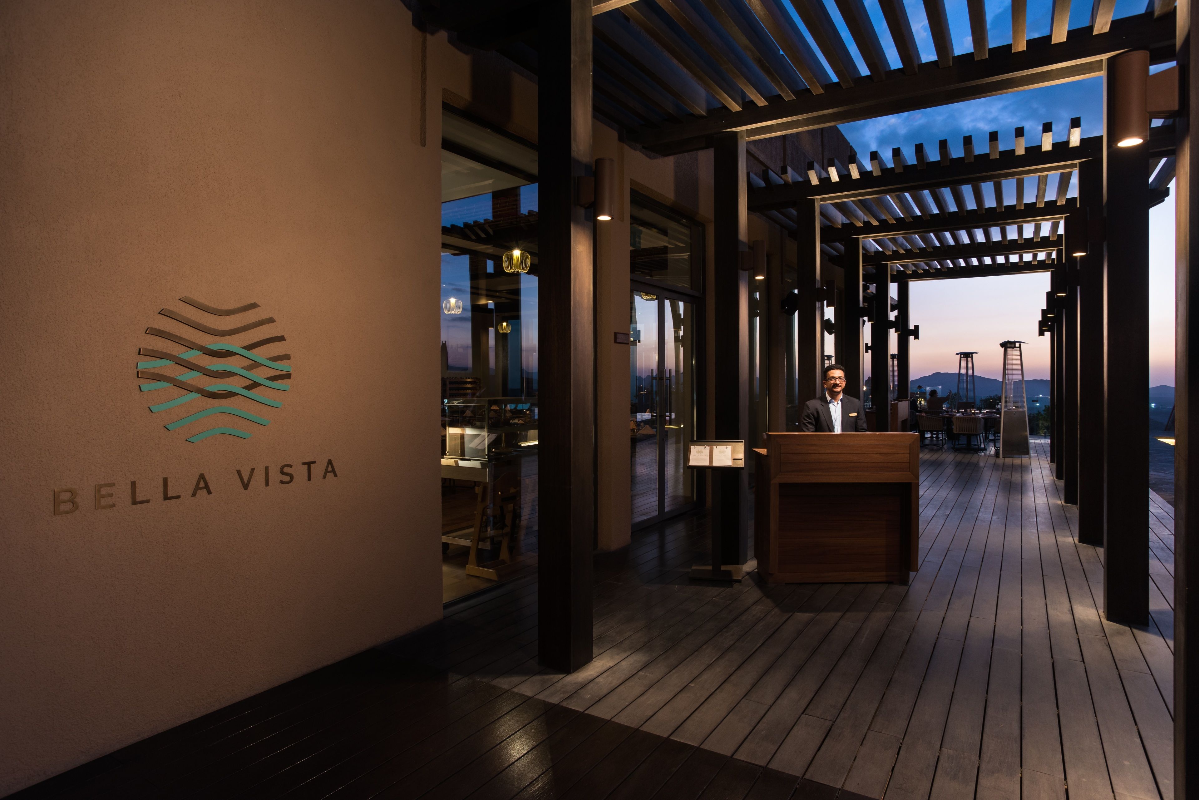 The entrance of Bella Vista with a reception desk, wooden flooring, and a view of the cityscape at dusk.