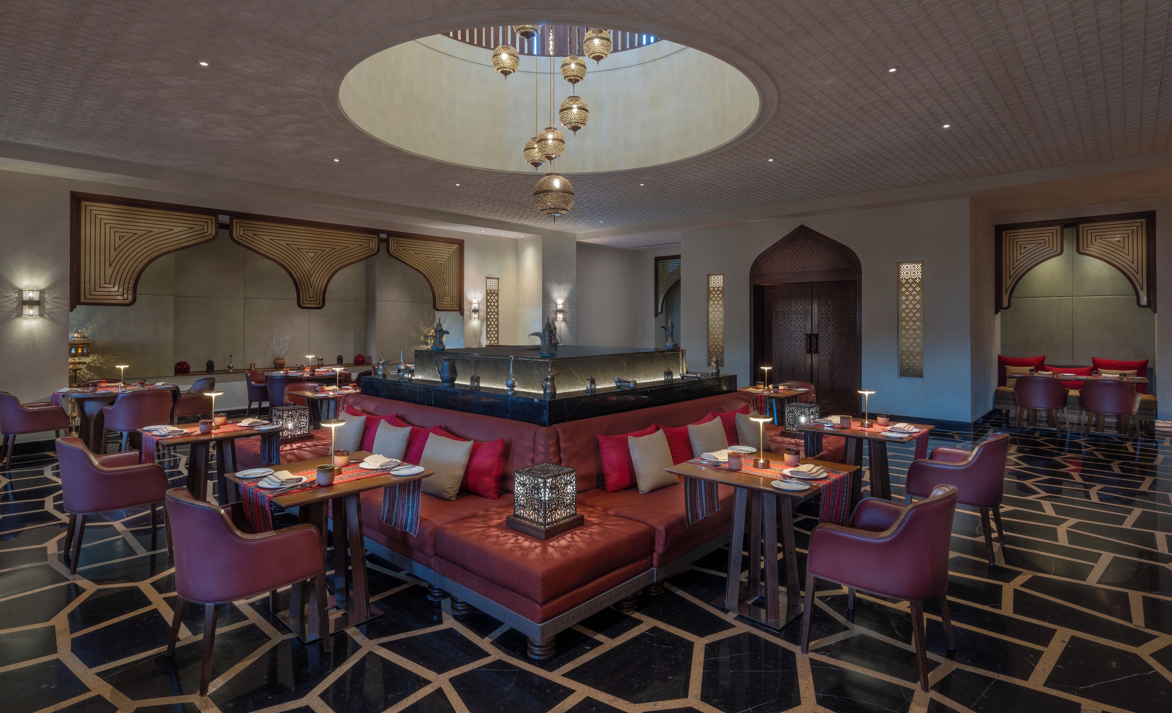 A modern interior with a central seating area, multiple tables, and a decorative ceiling.