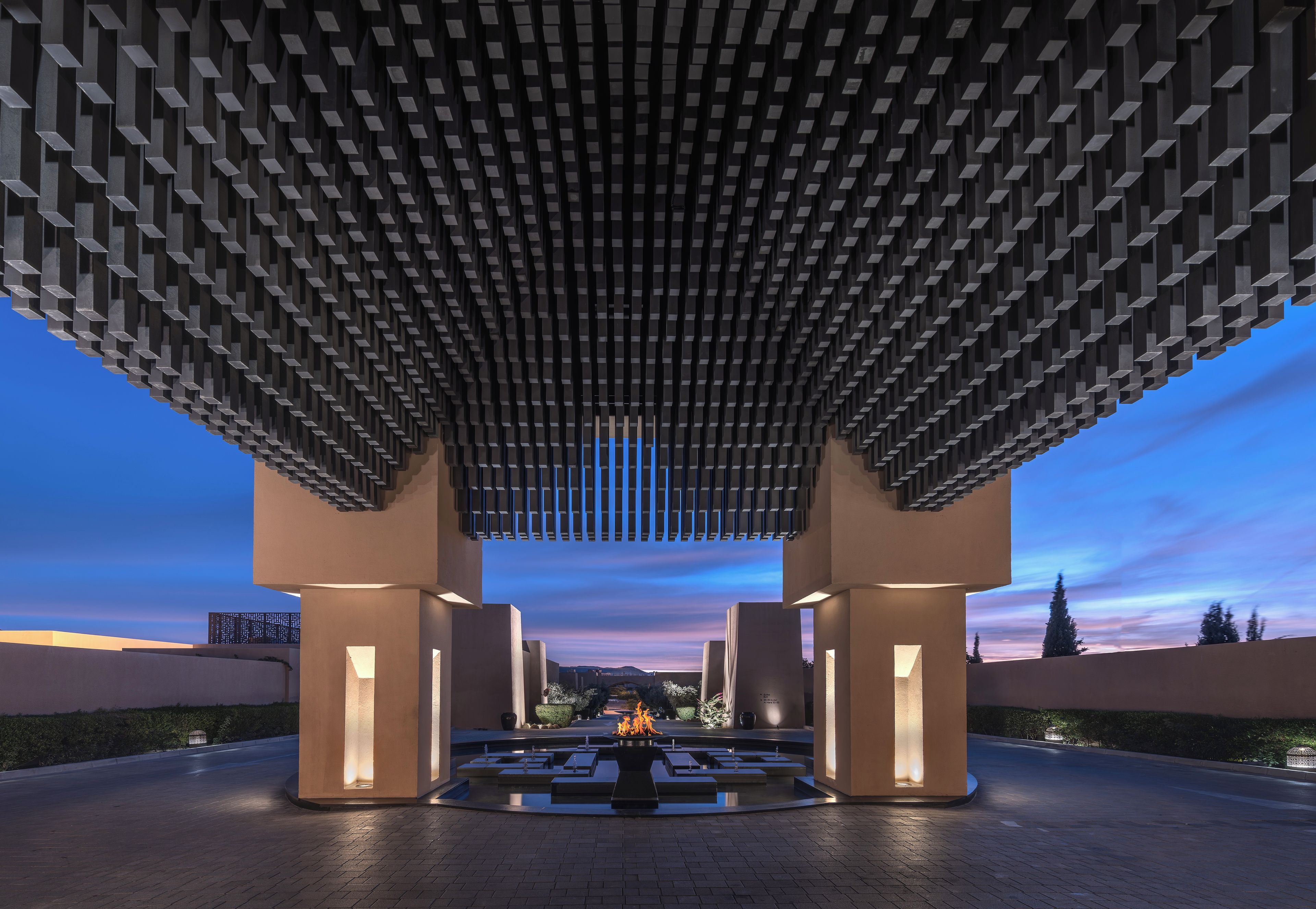 A modern architectural structure with a geometric design, featuring a central water feature and a series of illuminated columns.