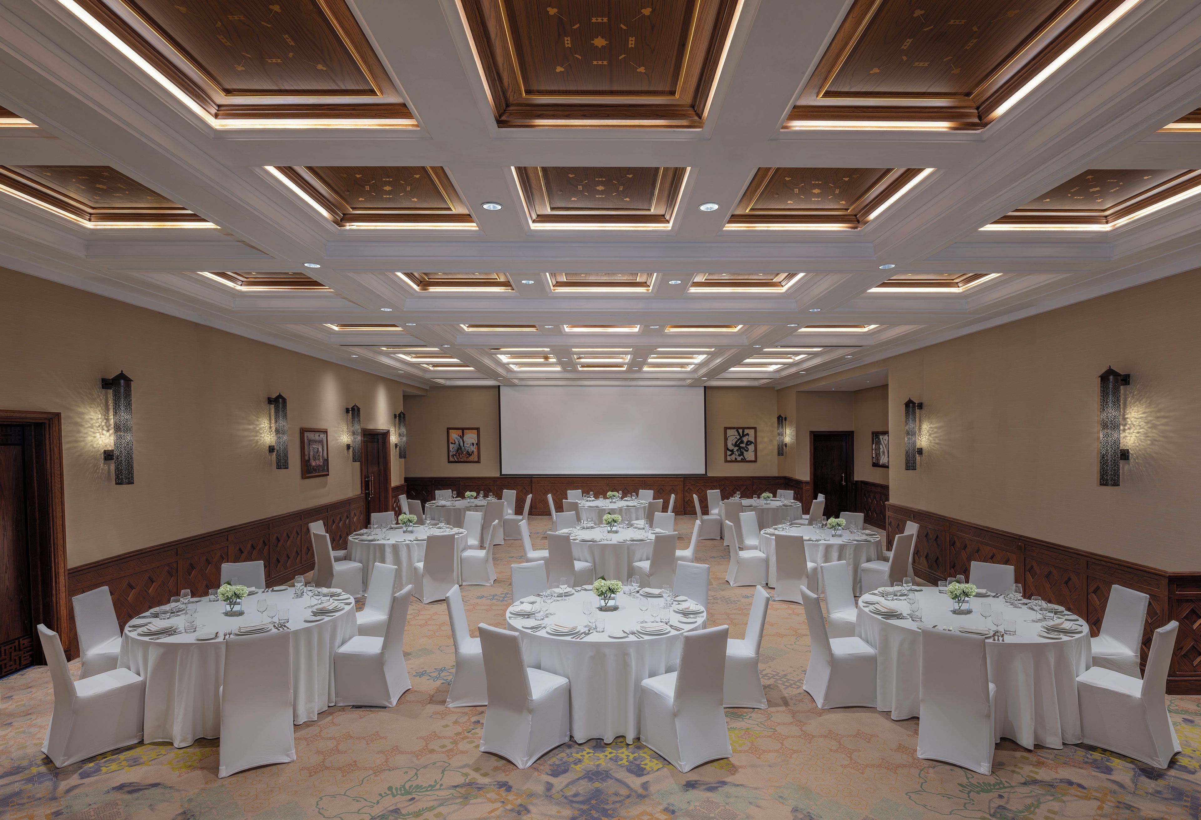A conference room with multiple round tables, white chairs, and a large screen at the front.