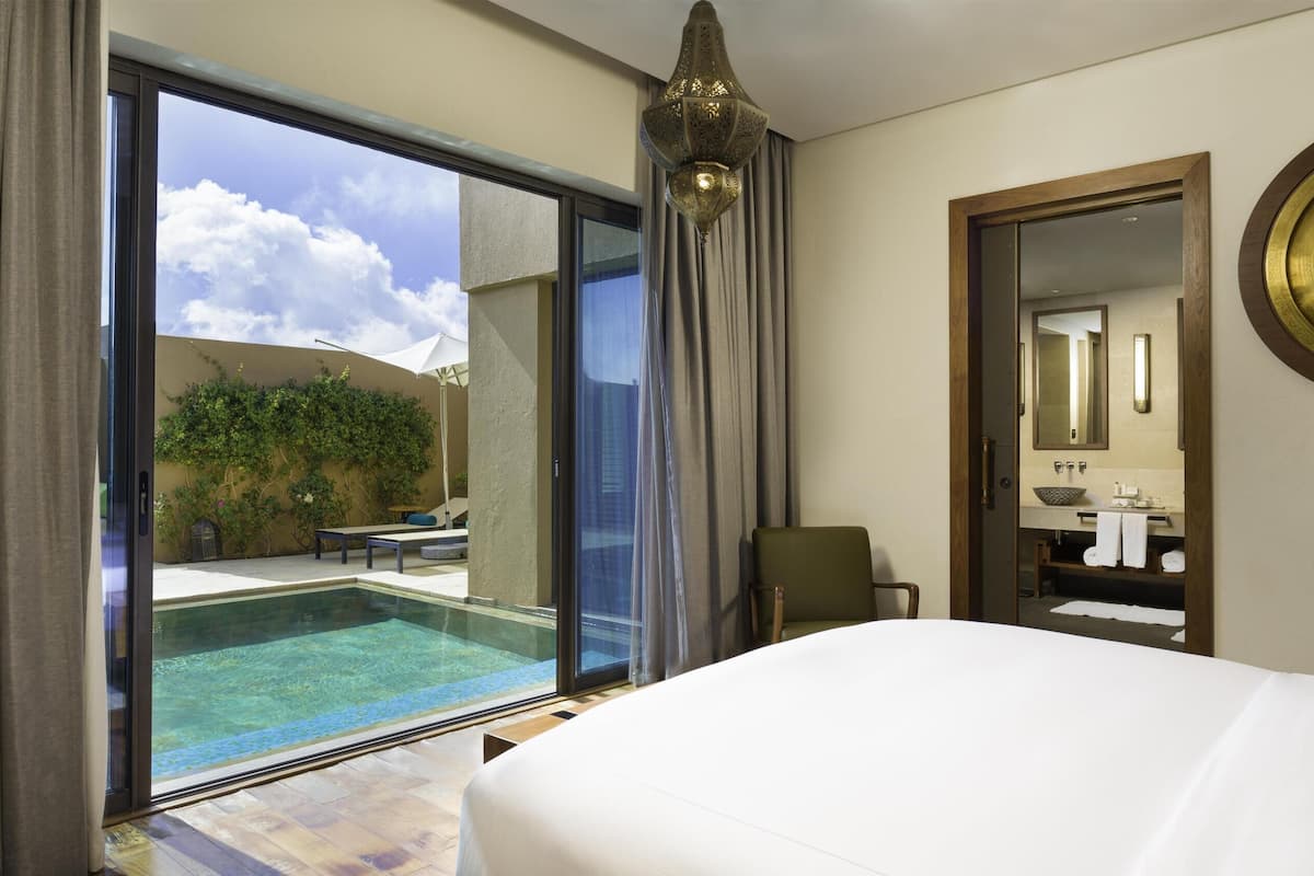 A hotel room with a large bed, a television, a view of an outdoor swimming pool, and a bathroom with a mirror and sink.