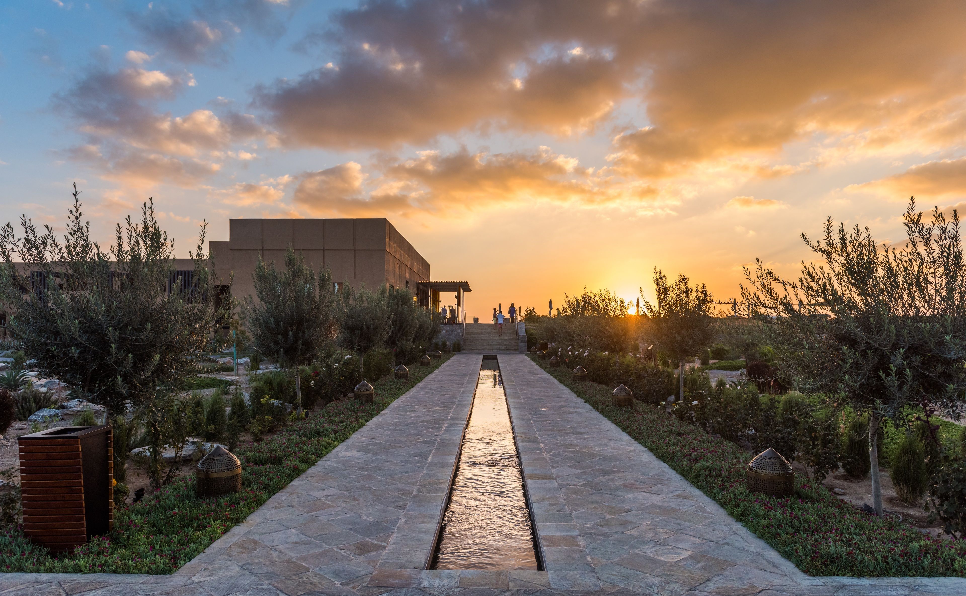 A pathway leading to a modern building with a flat roof, surrounded by landscaped gardens and trees.