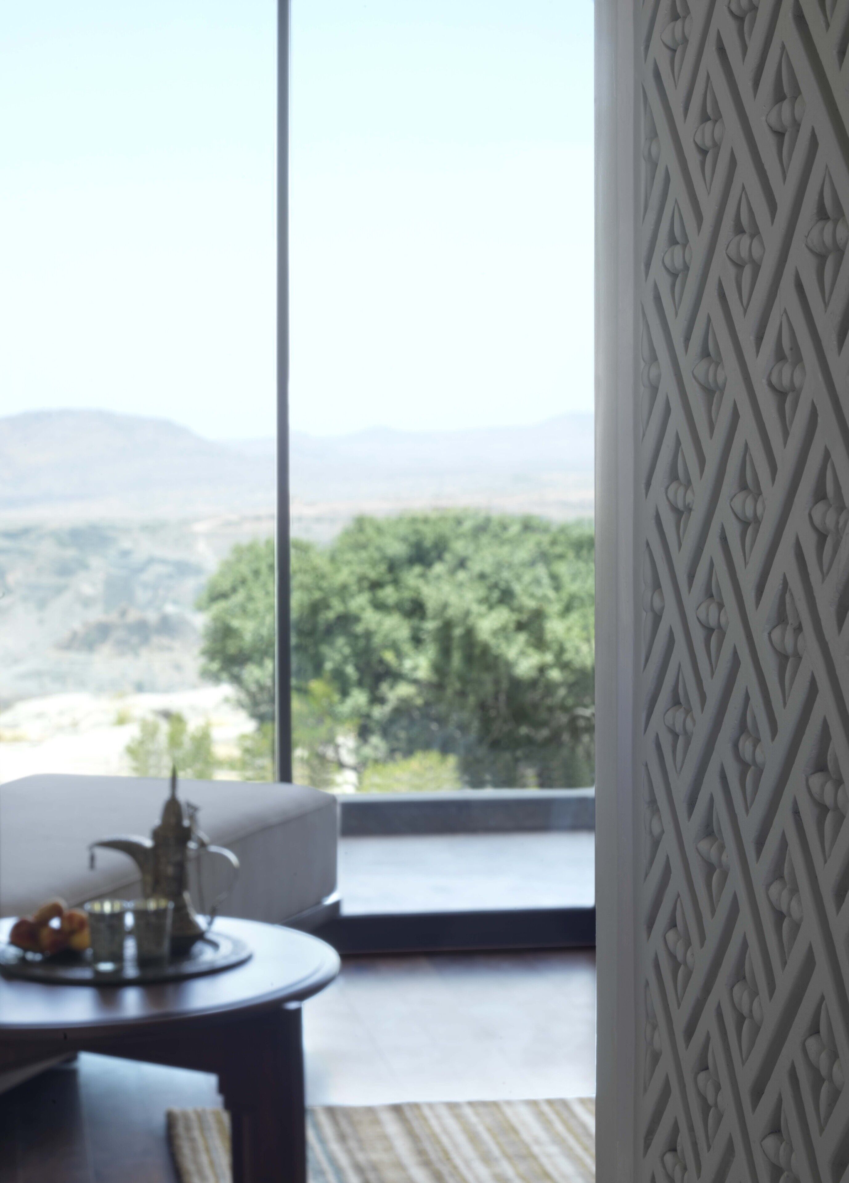Habitación con un ventanal grande que ofrece vistas a un paisaje montañoso. Se observa una mesa con un objeto decorativo y un candelabro.