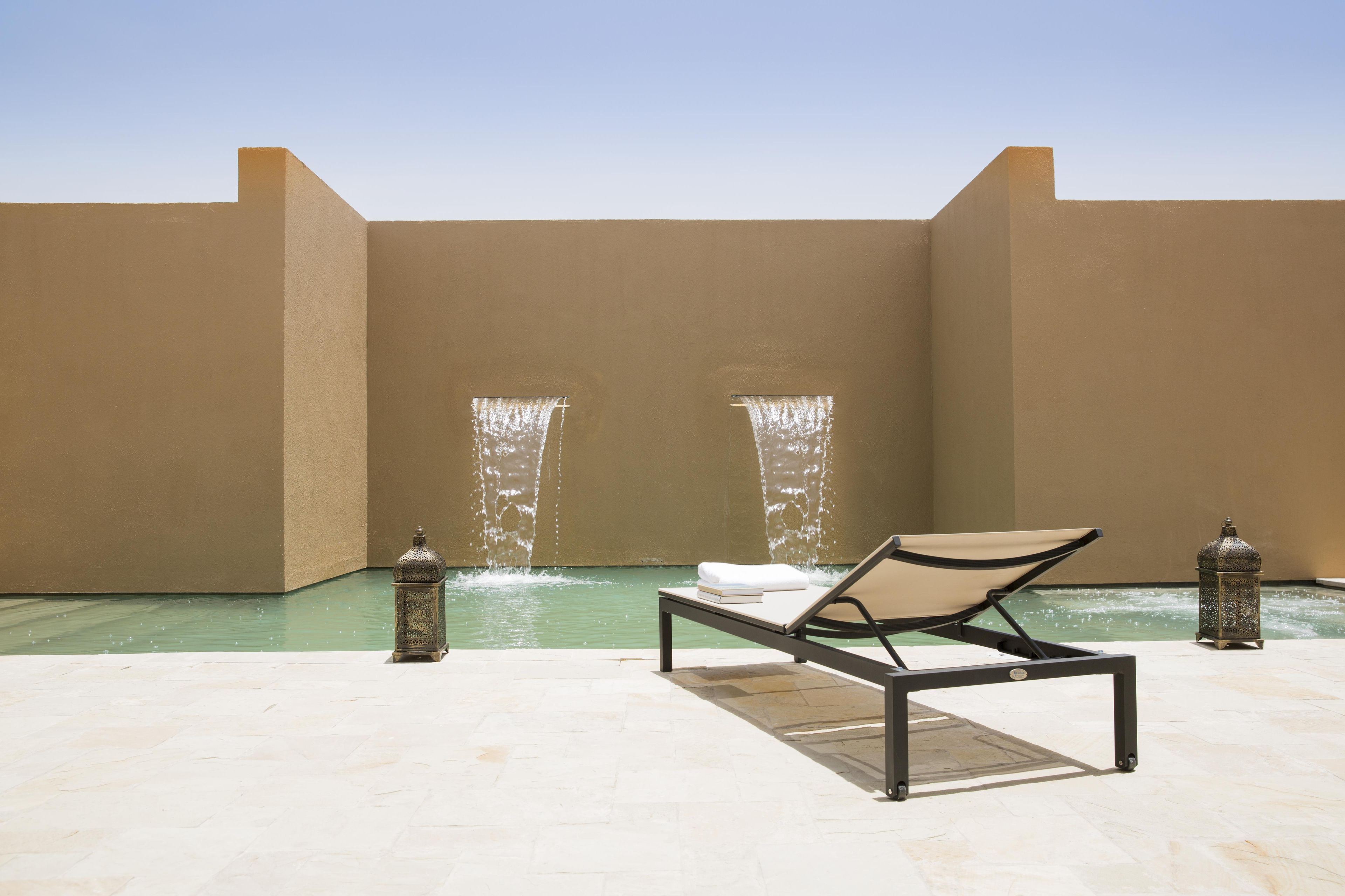 Un espace extérieur ensoleillé avec une piscine, un fauteuil de relaxation et deux éléments décoratifs aquatiques.
