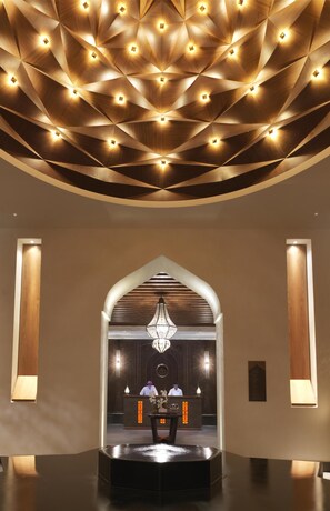 A lobby with a modern ceiling design, a reception desk, and a chandelier.