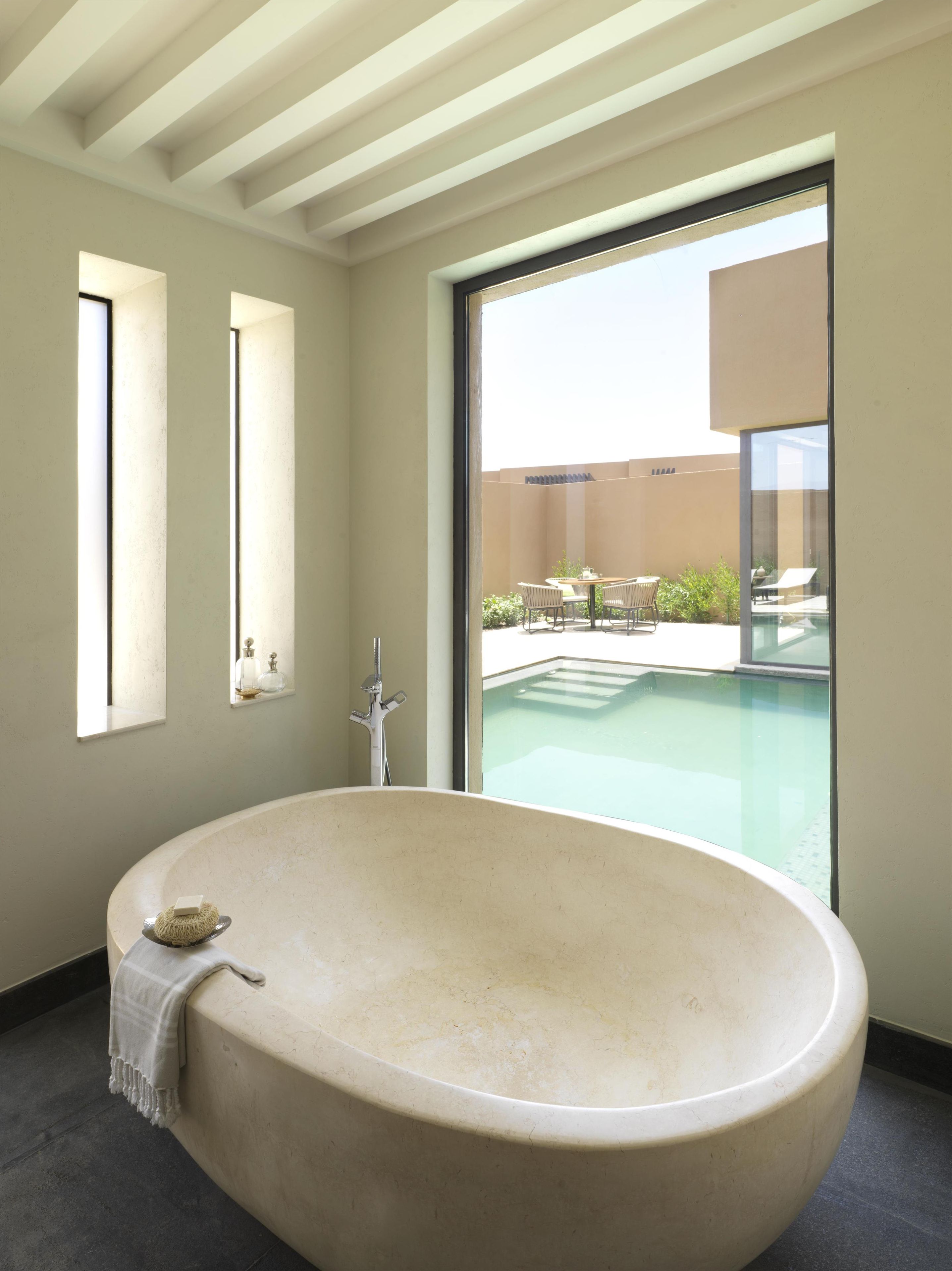 Un baño moderno con una bañera independiente, un ventanal y vistas a un área de piscina al aire libre.