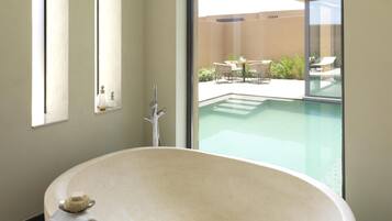 Un baño moderno con una bañera independiente, un ventanal y vistas a un área de piscina al aire libre.