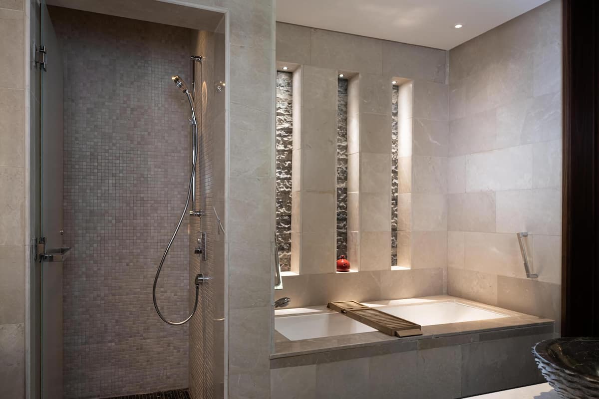 A modern bathroom with a shower, a bathtub, and a window with a stone wall.