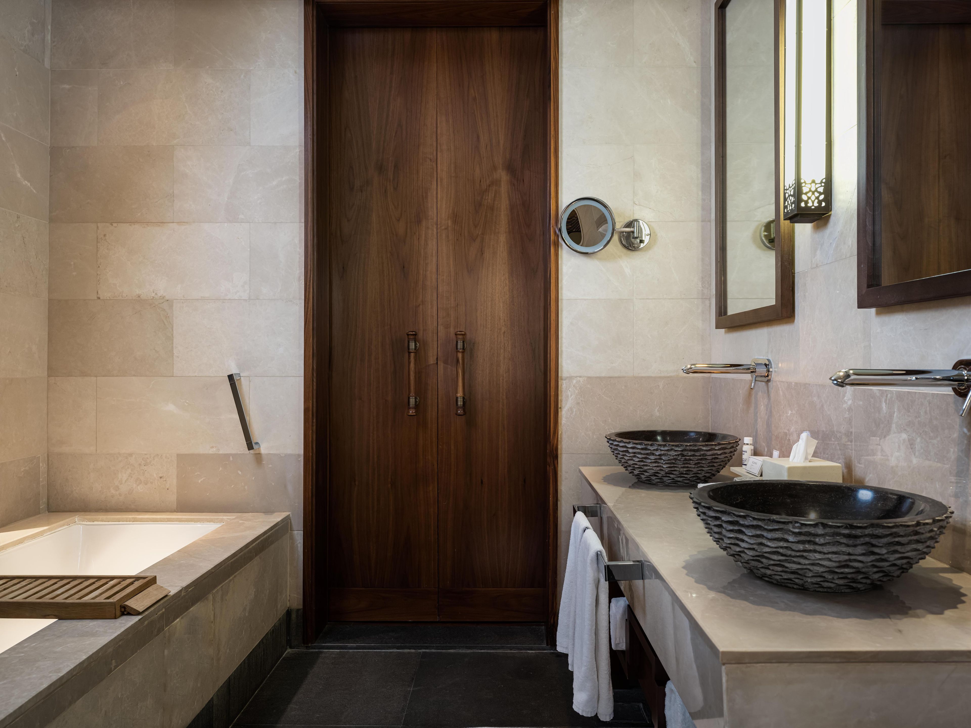 Une salle de bain moderne avec une porte en bois, une baignoire, un lavabo doté d’un grand bac et un miroir.