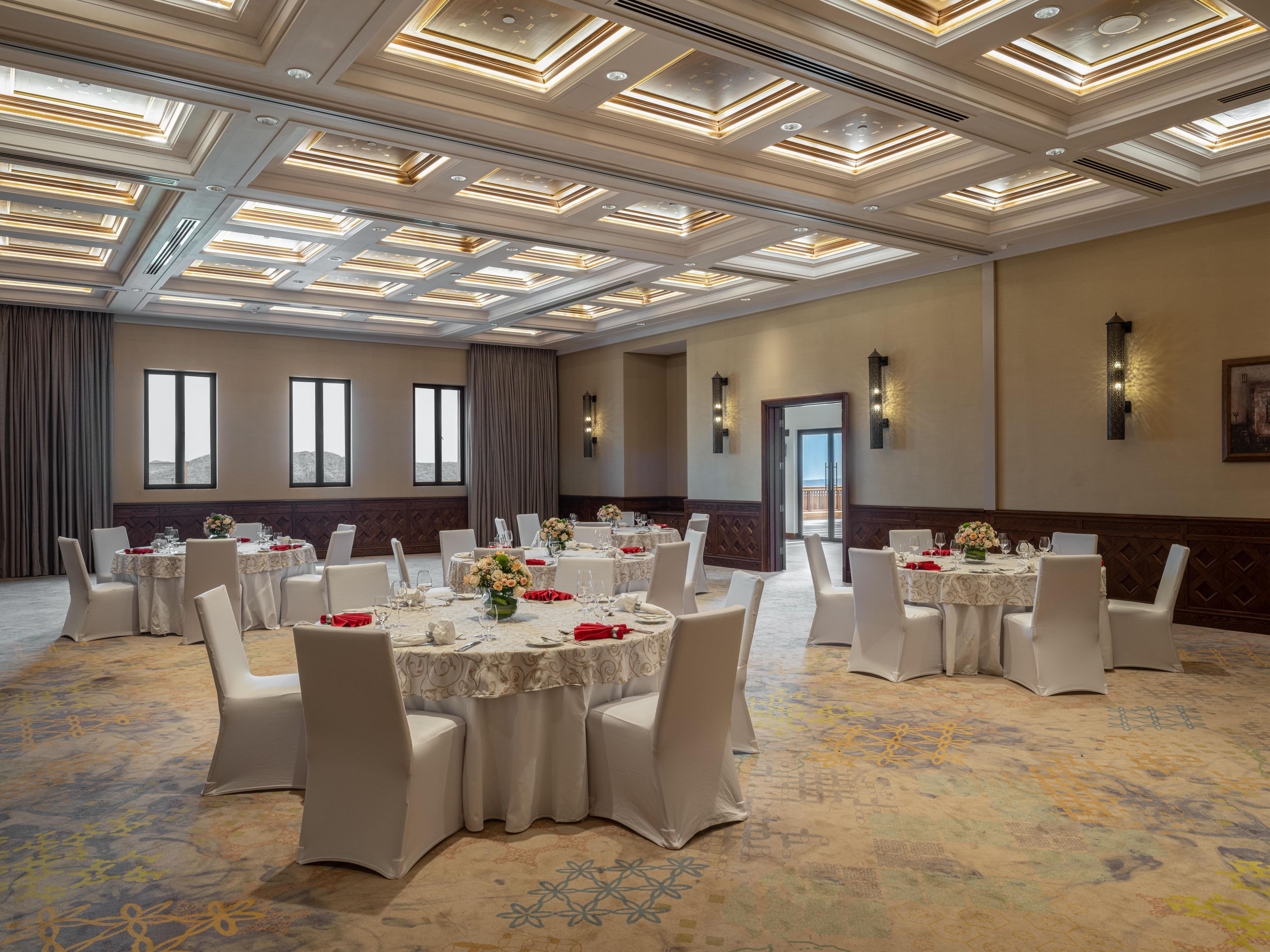 A banquet hall with round tables, white chairs, and a patterned carpet.