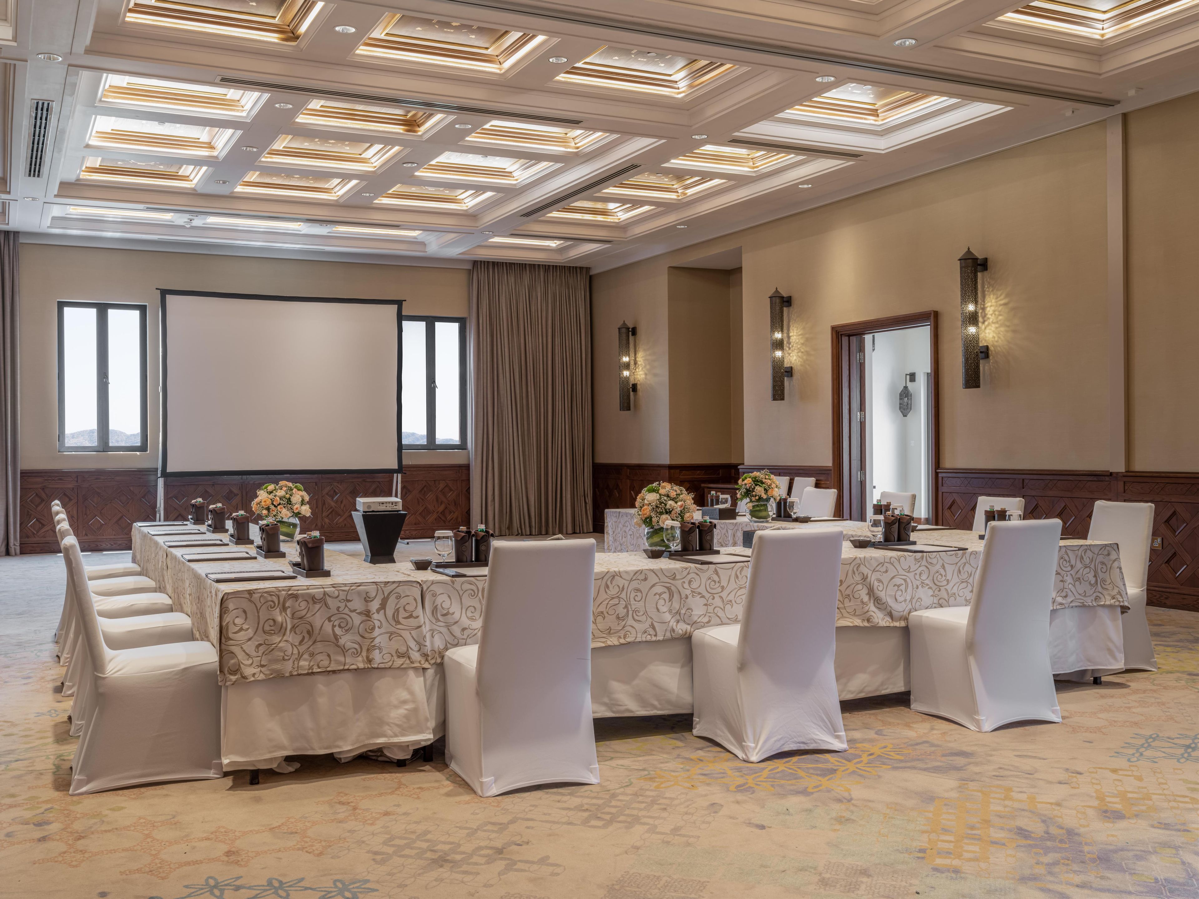 A conference room with a long table, chairs, and a projector screen.