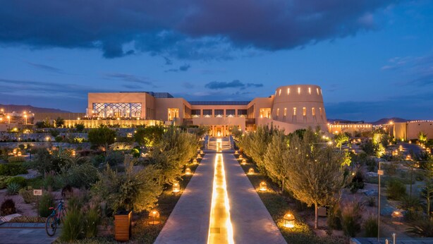 Un hotel moderno con un cortile interno, un edificio imponente caratterizzato da una struttura circolare unica e un vialetto ben illuminato che conduce all'ingresso.