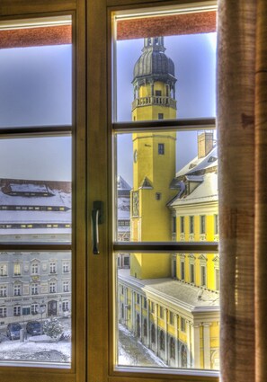 A view through a window of a yellow building with a tower, a snow-covered street, and a classical building with columns. - Zum Handtuch (Bautzen)