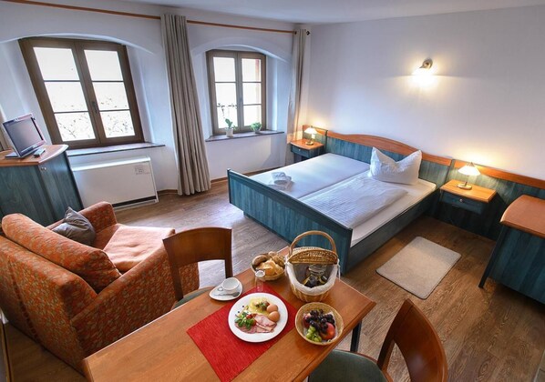 A hotel room with a bed, a desk, a chair, a sofa, and a dining table with breakfast items. - Zum Handtuch (Bautzen)