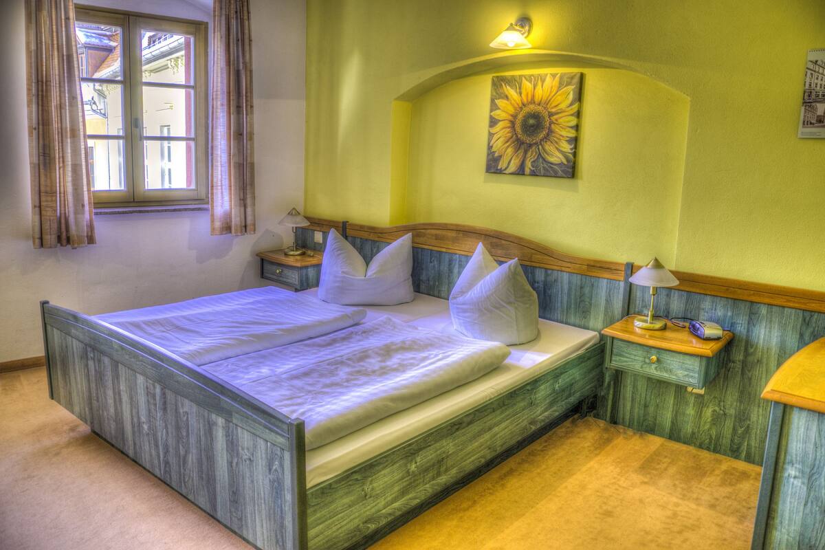 A bedroom with a wooden bed, a nightstand, a lamp, and a window with curtains.