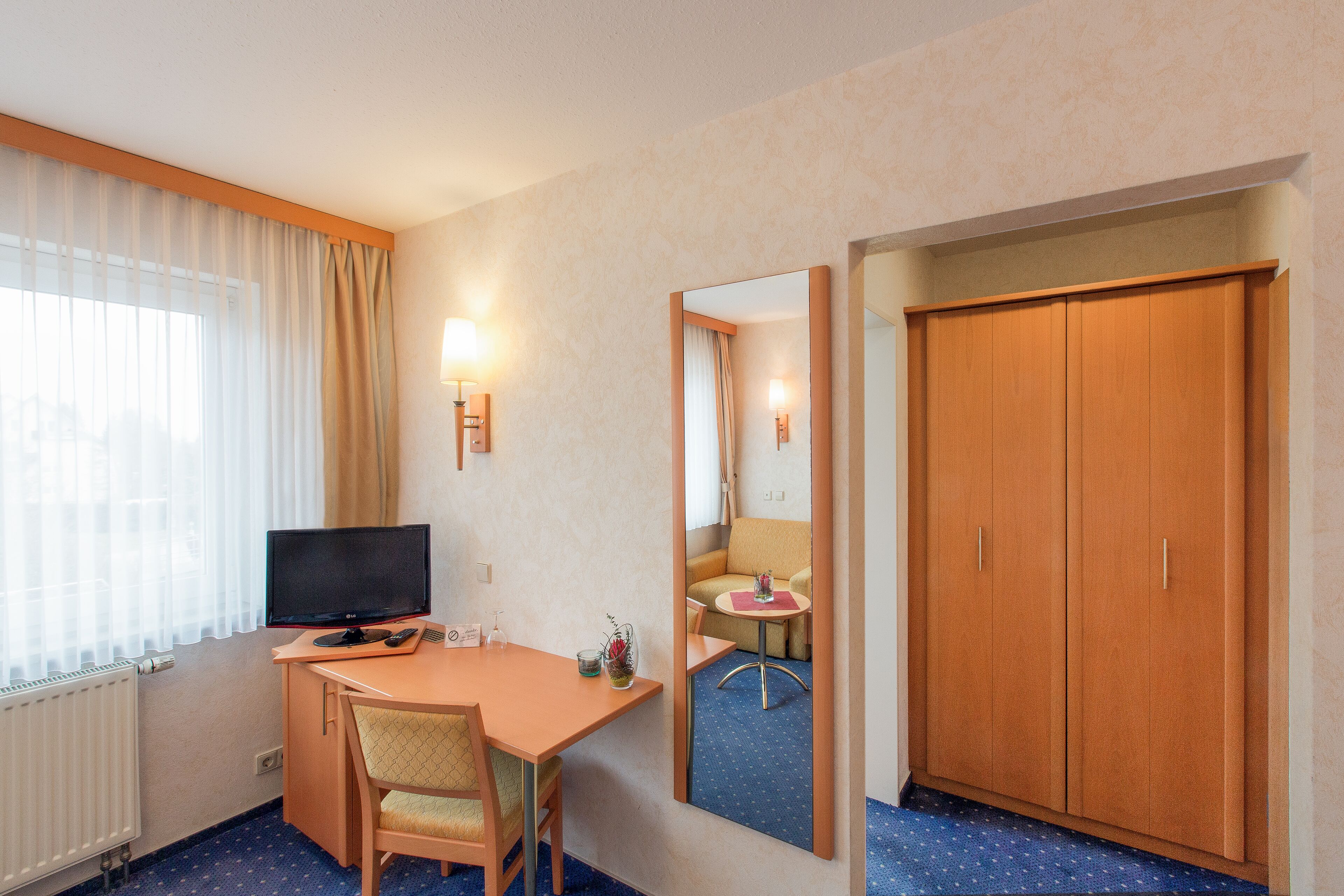 Una camera d'albergo con una scrivania, una sedia, televisione e un armadio.