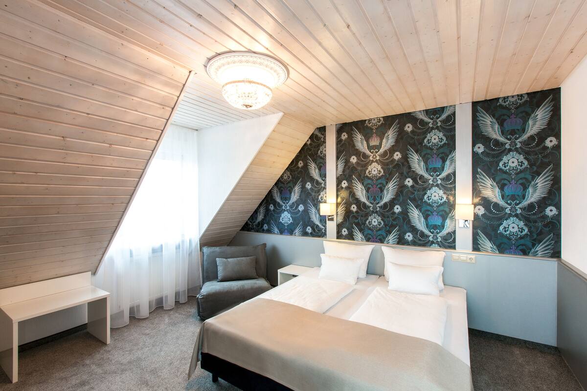 Un dormitorio con techo inclinado, una cama grande, un banco y una pared con un diseño decorativo.