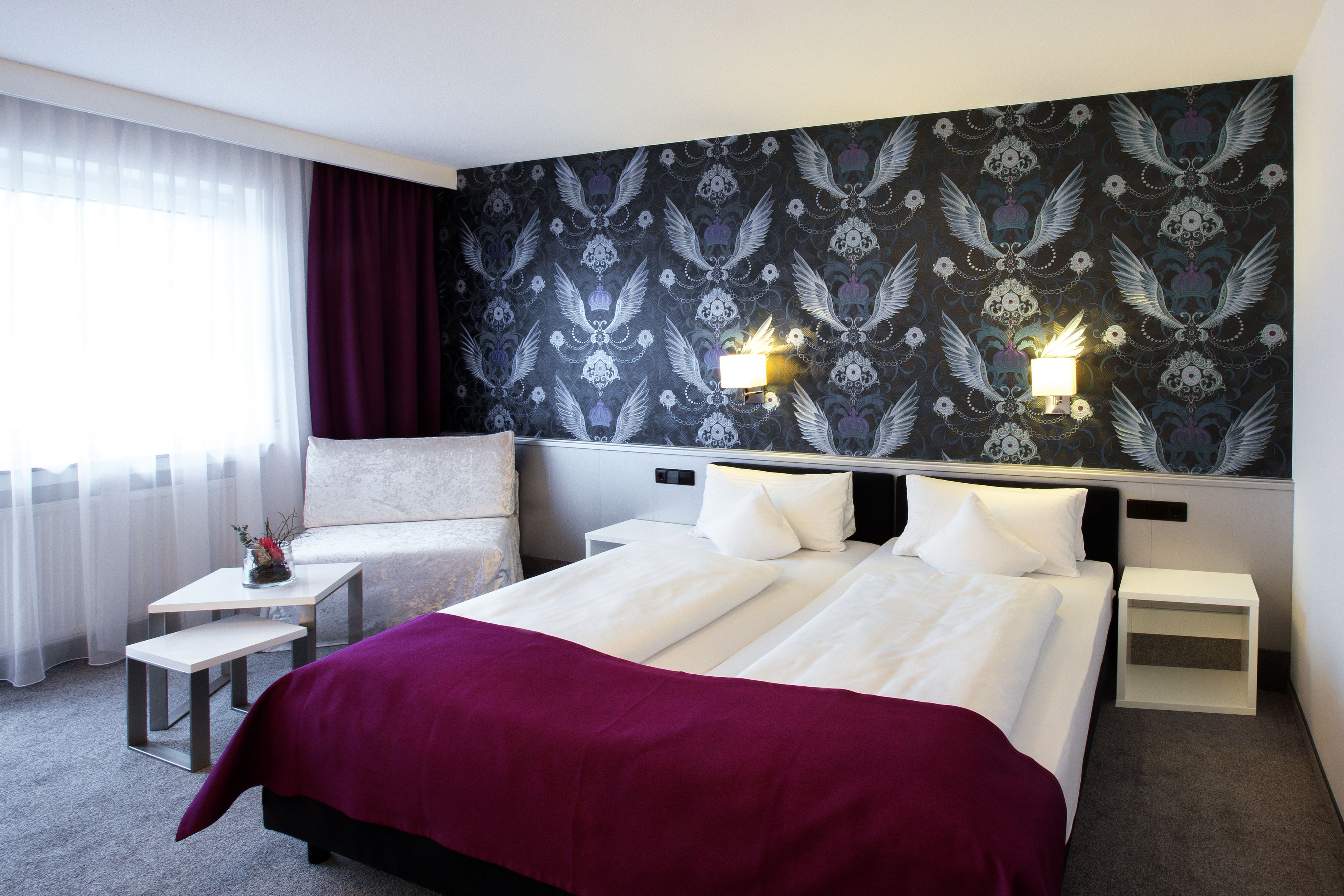 Ein Hotelzimmer mit einem großen Bett, zwei Nachttischen, einem kleinen Schreibtisch, einem Stuhl und einem Fenster mit Vorhängen.