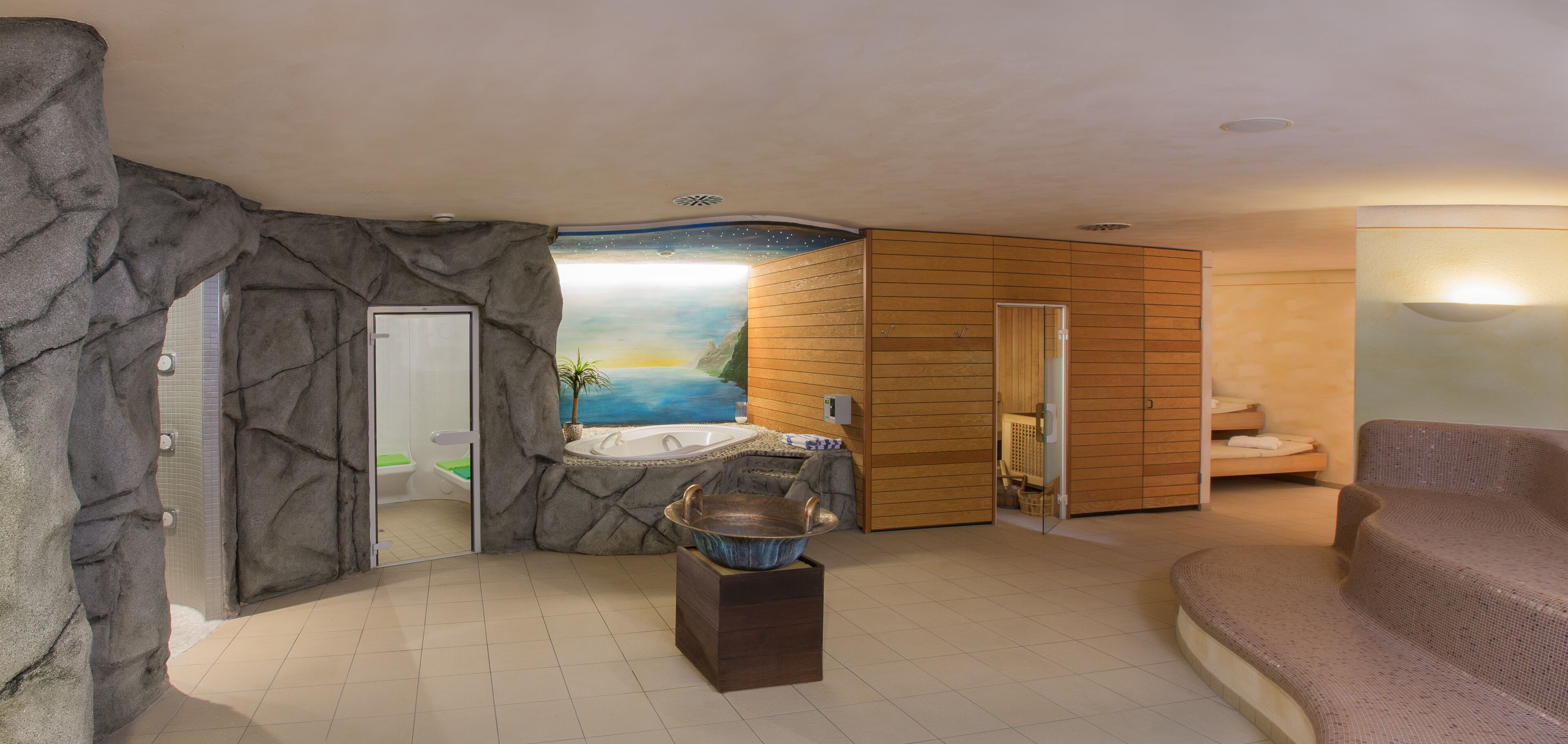 A spa room with a hot tub, wooden panel walls, a stone wall, and a view of a sunset over water.