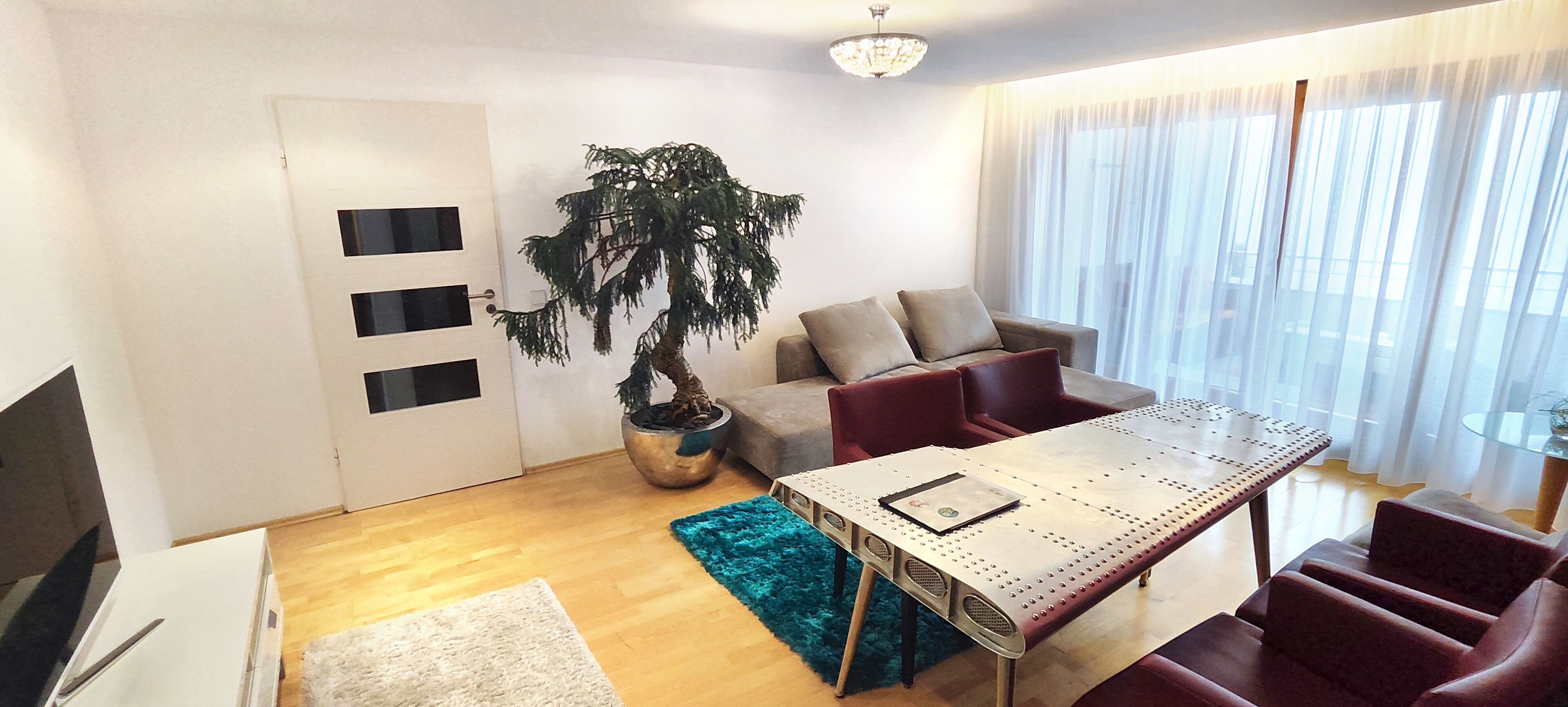 A modern living room with a dining table, sofa, and a large potted plant.
