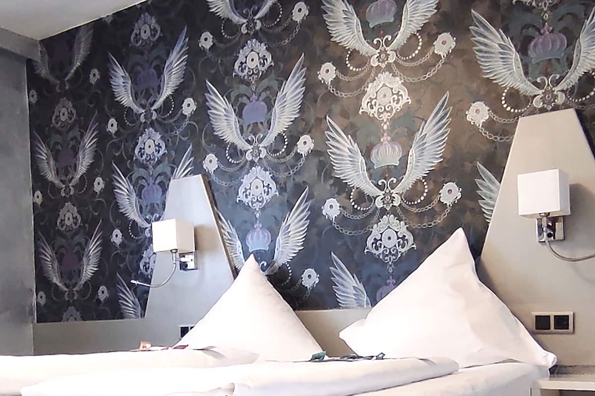Un dormitorio moderno con una cama grande, dos lámparas de noche y un papel tapiz floral con motivos de alas.