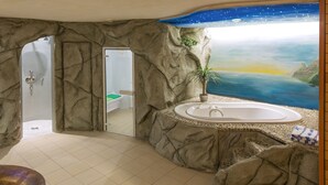 A bathroom with a rock-like wall design, a bathtub, and a shower area. - Hotel Hellers Twenty Four 2 (Friedrichshafen)
