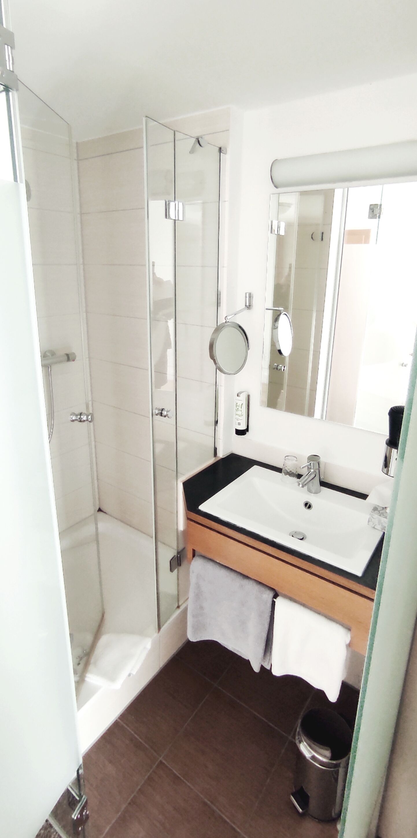 Ein modernes Badezimmer mit einer einbauartigen Duschkabine, einem Waschbecken mit Spiegel und einem Handtuchhalter.
