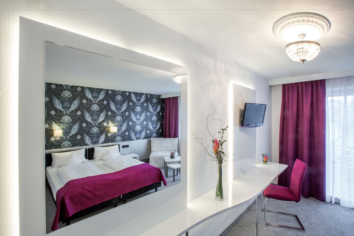 Una habitación de hotel con una cama grande, un escritorio, una silla, un televisor y un espejo.