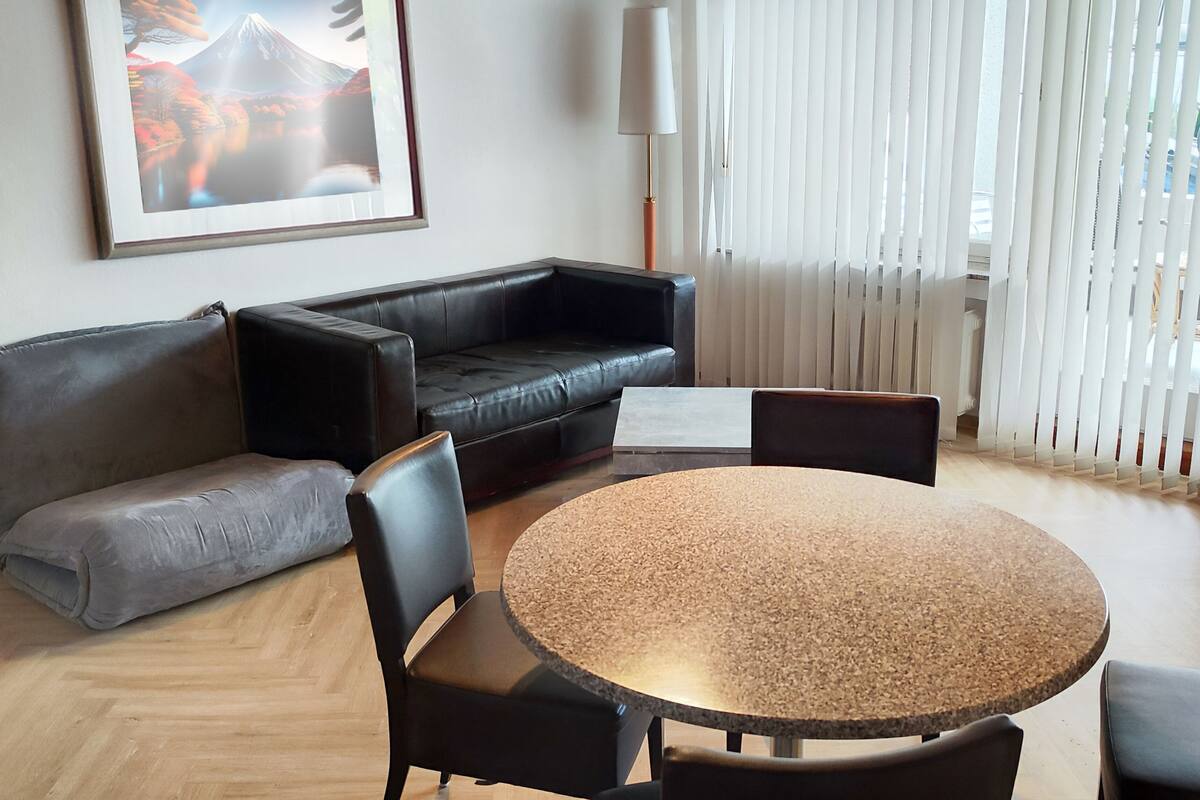 Una sala de estar moderna con un sofá de cuero negro, un sofá gris, una mesa de centro redonda y una mesa de comedor con sillas.