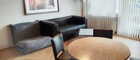 Una sala de estar moderna con un sofá de cuero negro, un sofá gris, una mesa de centro redonda y una mesa de comedor con sillas.