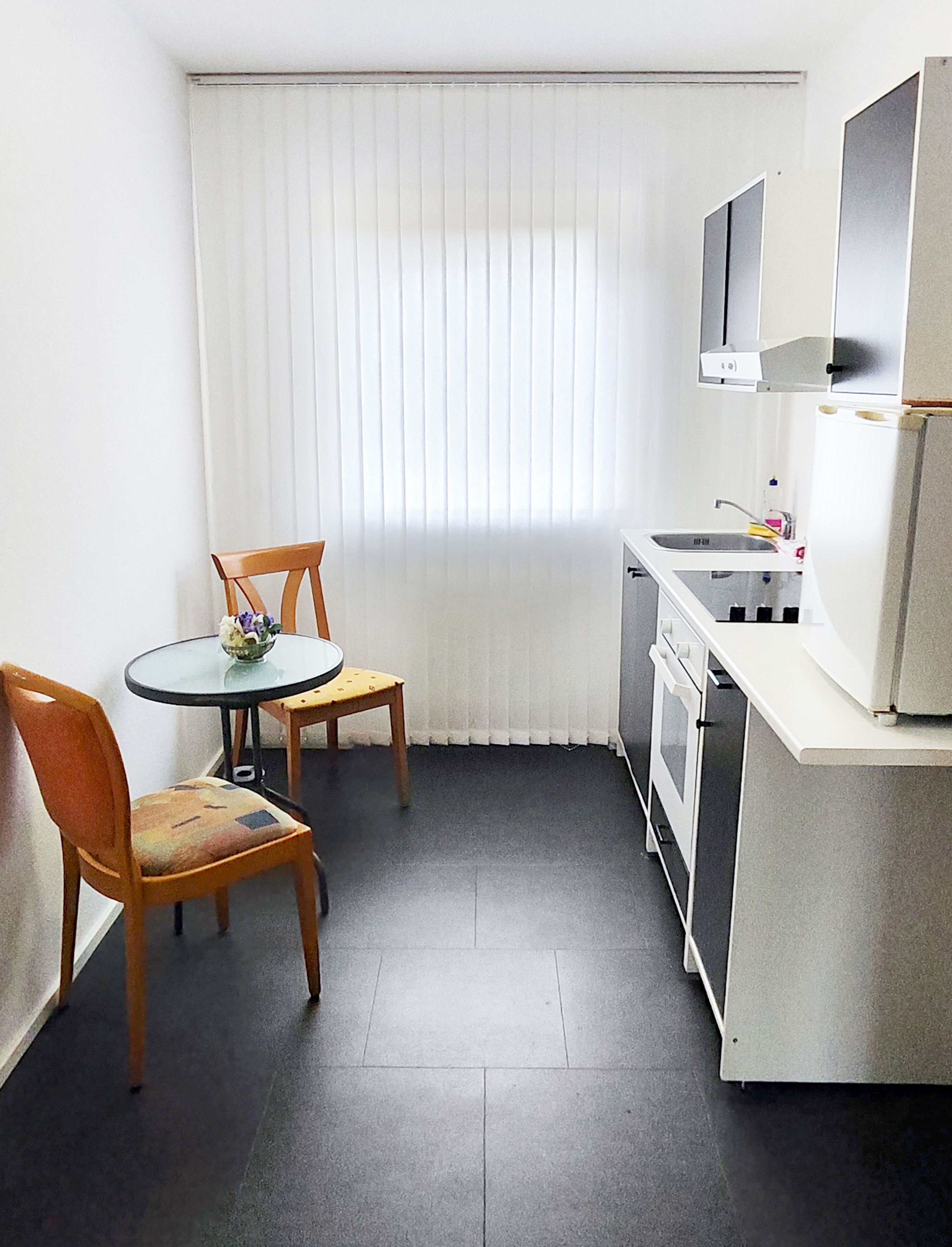 Una cocina compacta con una mesa de comedor y sillas, un refrigerador, un microondas y un lavamanos pequeño.