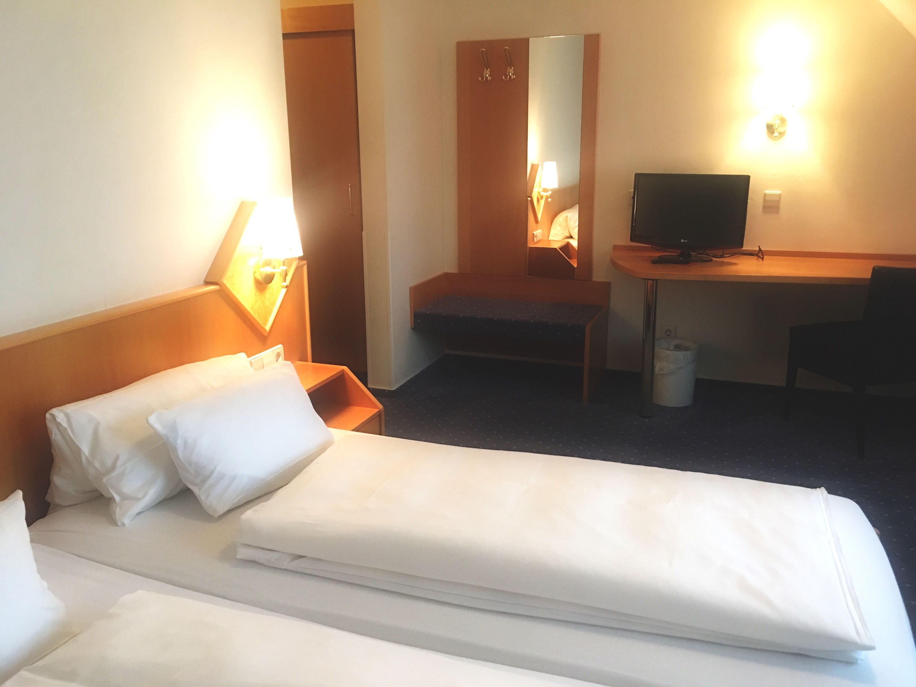 Une chambre d’hôtel avec deux lits, un bureau, une télévision et un miroir.