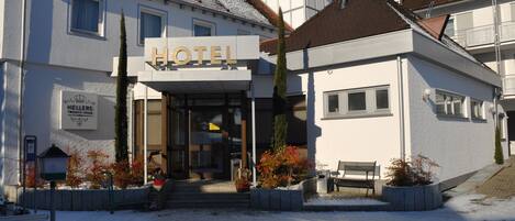 Un hotel con un cartel que dice “HOTEL” sobre la entrada. Hay escalones que llevan a la puerta, y un banco afuera.