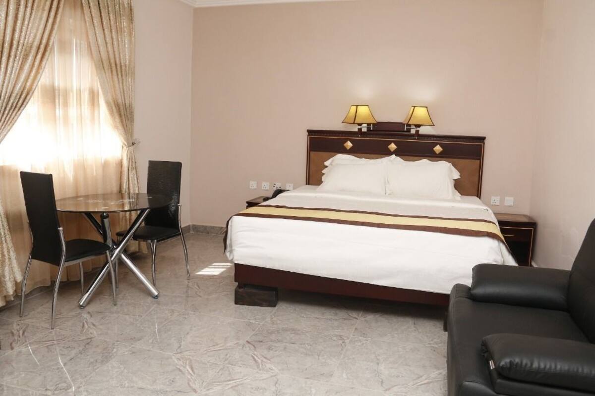 A hotel room with a bed, two bedside lamps, a desk with a chair, and a sofa.