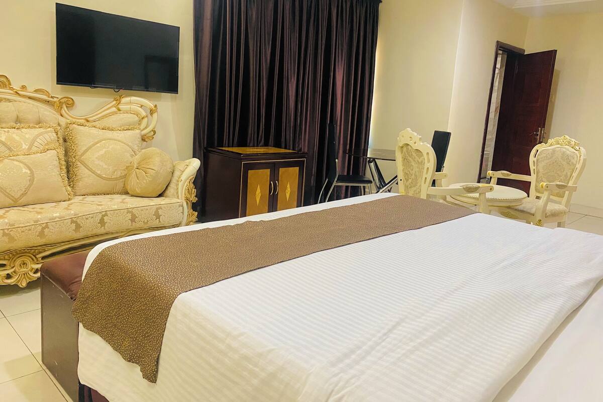 A hotel room with a bed, a sofa, a television, a small table, and a chair.