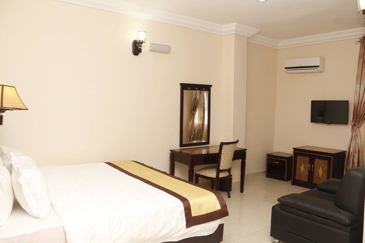 A hotel room with a bed, desk, chair, television, and an air conditioning unit.