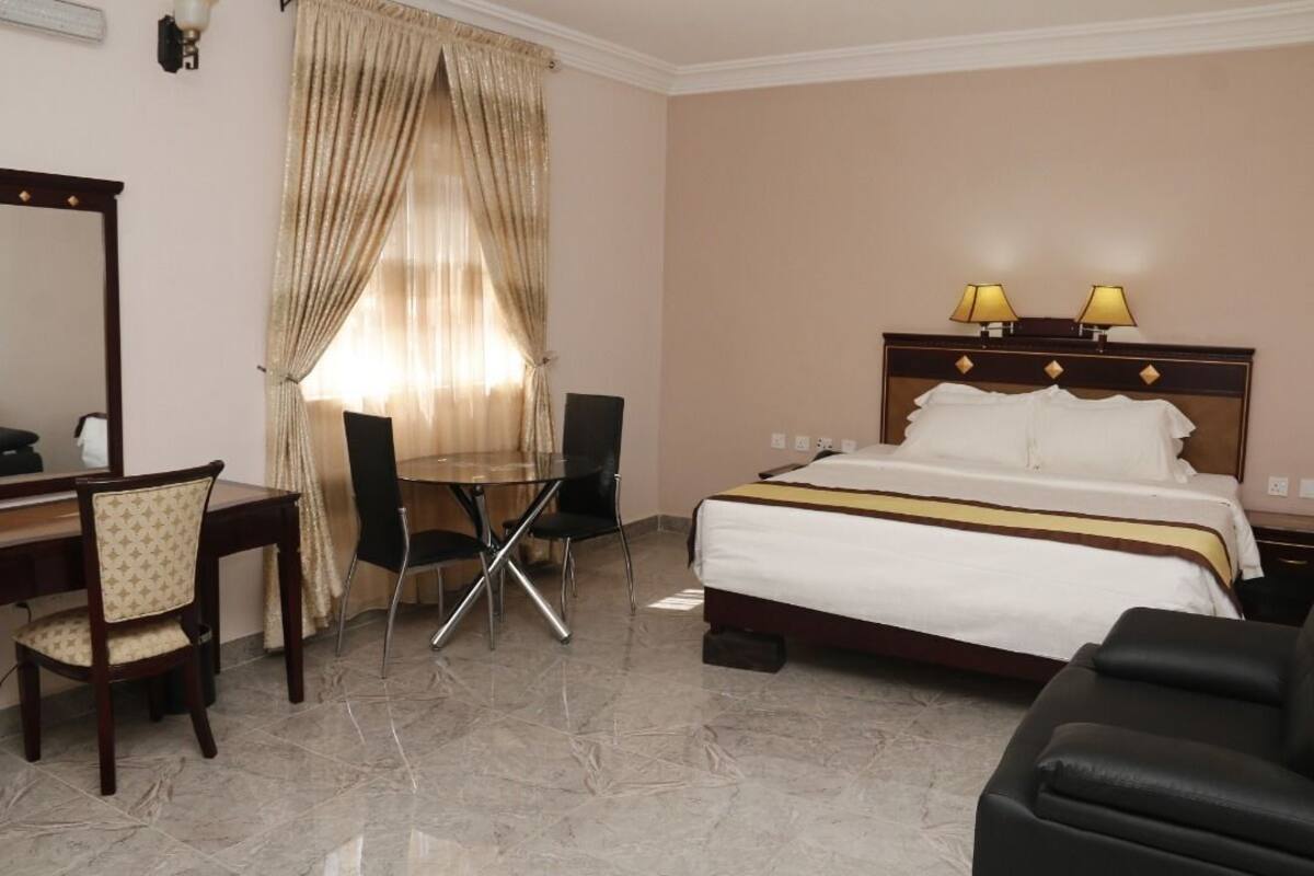 A hotel room with a bed, two bedside lamps, a desk with a chair, and a dining table.